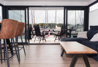 Modern houseboat living area with marina view, outdoor seating, and boats visible in the background, Germany.