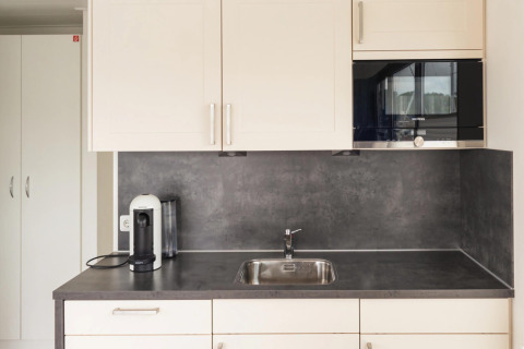 Modern houseboat kitchen with gray countertop, coffee machine, sink, and Siemens microwave in Germany.