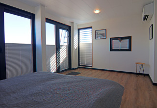 Modern bedroom interior with large windows, wooden floor, and simple decor on a houseboat in Germany.