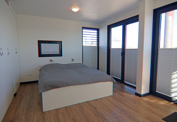 Bedroom on a houseboat with double bed, wooden floor, large windows, and cupboards at Family & Friends, Germany.
