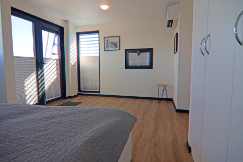 Bright, modern bedroom on a houseboat with large windows, wood flooring, and white cabinets in Germany.