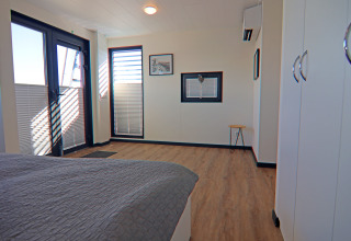 Bright, modern bedroom on a houseboat with large windows, wood flooring, and white cabinets in Germany.