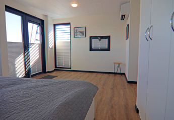 Modernes Schlafzimmer auf einem Hausboot mit großen Fenstern, Holzfußboden und weißen Schränken.