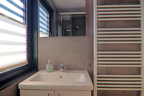 Modern houseboat bathroom with sink, mirror, towel heater, and large windows with blinds for natural light.