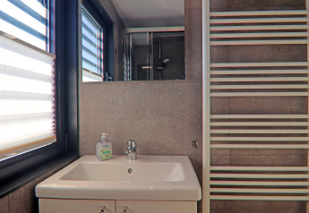 Moderne badkamer op woonboot met wastafel, spiegel, handdoekradiator en grote ramen met jaloezieën.