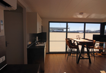 Intérieur moderne de péniche avec cuisine ouverte, table à manger, grandes fenêtres et vue sur l’eau.