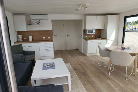 Intérieur moderne de péniche avec cuisine ouverte, coin salon, table à manger et grandes fenêtres.