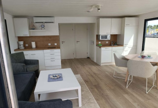 Intérieur moderne de péniche avec cuisine ouverte, coin salon, table à manger et grandes fenêtres.