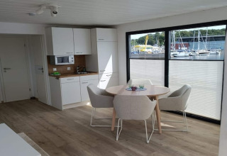 Intérieur de péniche moderne avec coin cuisine, salle à manger et grandes fenêtres donnant sur le port.