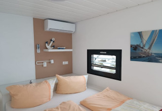 Chambre moderne sur une péniche avec fenêtre, tableau de voilier et oreillers pastel clairs.