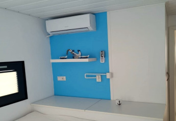 Modern interieur van een woonboot met blauwe muur, airco, plank met decoraties en afstandsbediening.
