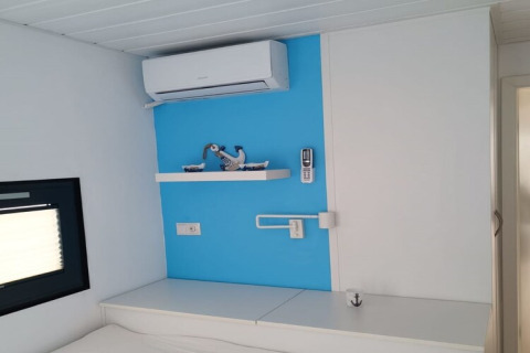 Intérieur moderne de péniche avec mur bleu, climatisation, étagère décorative et télécommande.