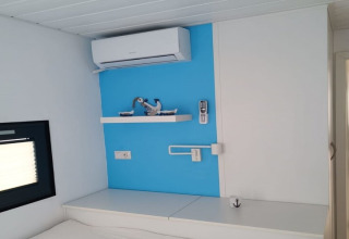 Intérieur moderne de péniche avec mur bleu, climatisation, étagère décorative et télécommande.