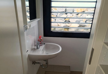 Kleine badkamer op woonboot met wastafel, spiegel en uitzicht op stenen door het raam in Duitsland.