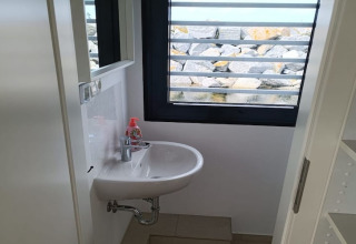 Kleine badkamer op woonboot met wastafel, spiegel en uitzicht op stenen door het raam in Duitsland.