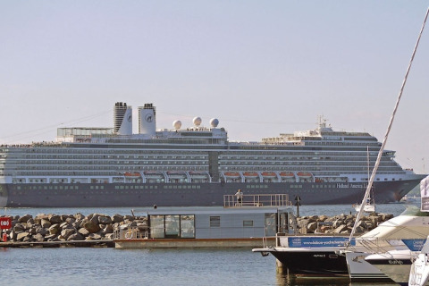 Photo d'une péniche au bord de l'eau avec un grand paquebot de croisière Holland America Line derrière.