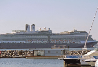 Photo d'une péniche au bord de l'eau avec un grand paquebot de croisière Holland America Line derrière.