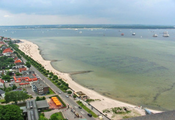 Uitzicht vanaf een woonboot op een zandstrand, rustige kustlijn en boten in Duitsland onder bewolkte hemel.