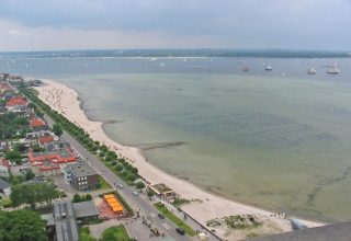 Udsigt over en sandstrand og kyst med både i havnen, set fra et husbåd i Tyskland under overskyet himmel.