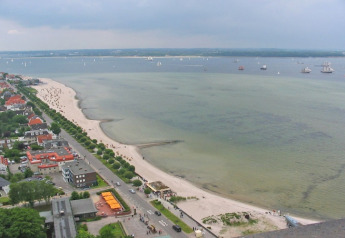 Uitzicht vanaf een woonboot op een zandstrand, rustige kustlijn en boten in Duitsland onder bewolkte hemel.