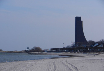 Sandy beach scene with a unique tall tower, gentle waves, and nearby buildings by a houseboat location.