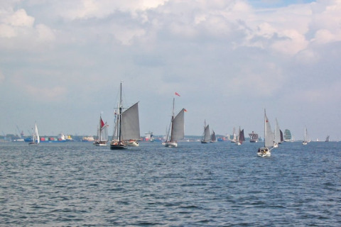 Voiliers et bateaux sur l’eau, vus depuis une péniche, avec un ciel nuageux et un port en arrière-plan.