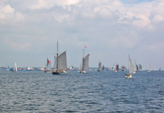 Voiliers et bateaux sur l’eau, vus depuis une péniche, avec un ciel nuageux et un port en arrière-plan.