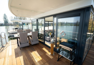 Terraza con comedor al aire libre en una casa flotante moderna en Höxter, con vista al agua tranquila.