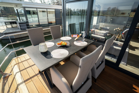Zona de comedor al aire libre en una casa flotante en Höxter con seis sillas y mesa negra junto al río.