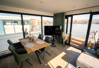 Moderne woon- en eetruimte op een woonboot in Höxter met zicht op het water door grote ramen.