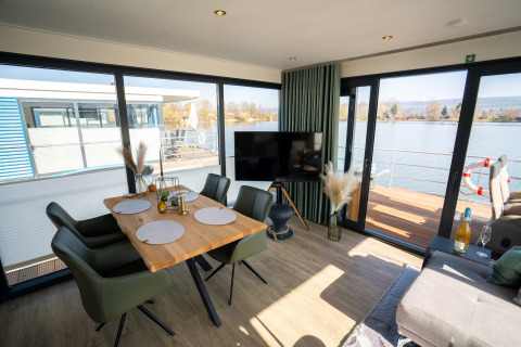 Moderne woon- en eetruimte op een woonboot in Höxter met zicht op het water door grote ramen.