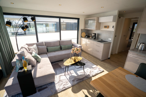 Soggiorno e cucina moderni su una houseboat a Höxter con ampie finestre, divano e tavolo da pranzo.