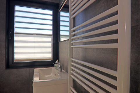 Bathroom on a houseboat in Germany, showing a sink, towel radiator, and large window with striped blinds.