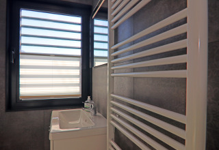 Bathroom on a houseboat in Germany, showing a sink, towel radiator, and large window with striped blinds.