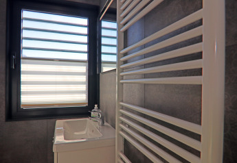 Badezimmer auf dem Hausboot mit Waschbecken, modernen Armaturen, Handtuchheizkörper und Fenster mit Jalousien.