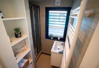 Moderne badeværelse på en husbåd i Höxter med brusekabine, håndvask, hylder og vindue med planter.