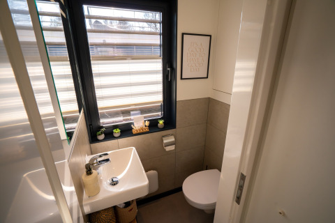 Moderne badeværelse på en husbåd i Höxter med vindue, lille håndvask, toilet og grønne dekorationer.