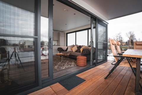 Vue d'une péniche moderne à Höxter avec portes vitrées ouvertes, terrasse en bois et salon confortable.