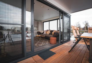 View of a modern houseboat in Höxter showing open glass doors, stylish deck seating, and cozy living room.