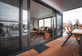 Vue d'une péniche moderne à Höxter avec portes vitrées ouvertes, terrasse en bois et salon confortable.