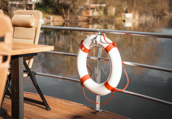 Reddingsboei aan de reling van een woonboot in Höxter met zicht op het water en beige stoelen buiten.