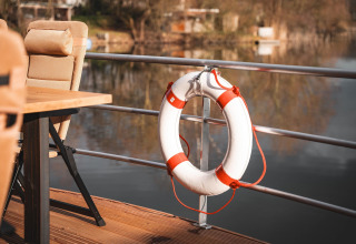 Lifebuoy hanging on railing of a houseboat in Höxter, overlooking calm water and comfortable chairs.