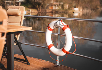 Bouée de sauvetage accrochée à la rambarde d'une péniche à Höxter, avec vue sur l'eau calme et les chaises.