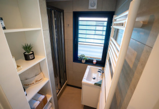 Baño moderno en una casa flotante en Höxter, Alemania, con ducha, ventana y estanterías con toallas y decoración.