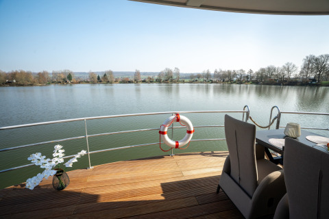 Vista desde la Houseboat en Höxter, terraza con salvavidas, flores en jarrón y sillas junto al lago.