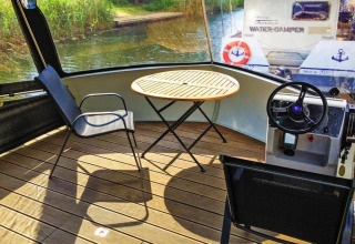 Zonnige zithoek met tafel, stoelen en stuurwiel op een Watercamper deluxe woonboot in Duitsland.
