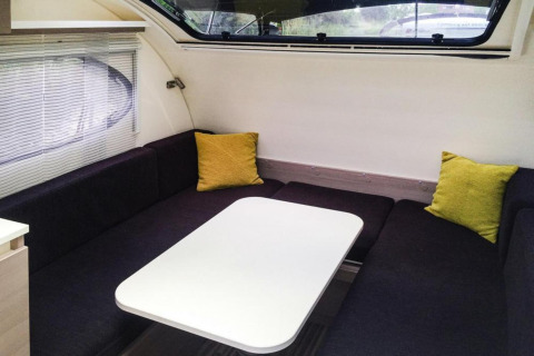 Moderne zithoek met donkere banken en gele kussens aan boord van de Watercamper deluxe in Duitsland.