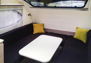 Moderne zithoek met donkere banken en gele kussens aan boord van de Watercamper deluxe in Duitsland.