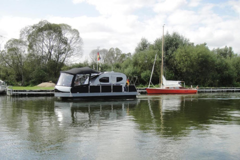 Foto van het huisboot Watercamper deluxe op het water in Duitsland, met bomen en een andere boot ernaast.