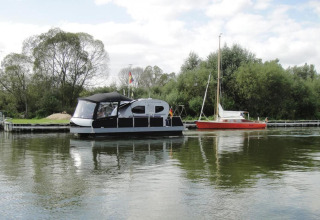 Foto van het huisboot Watercamper deluxe op het water in Duitsland, met bomen en een andere boot ernaast.